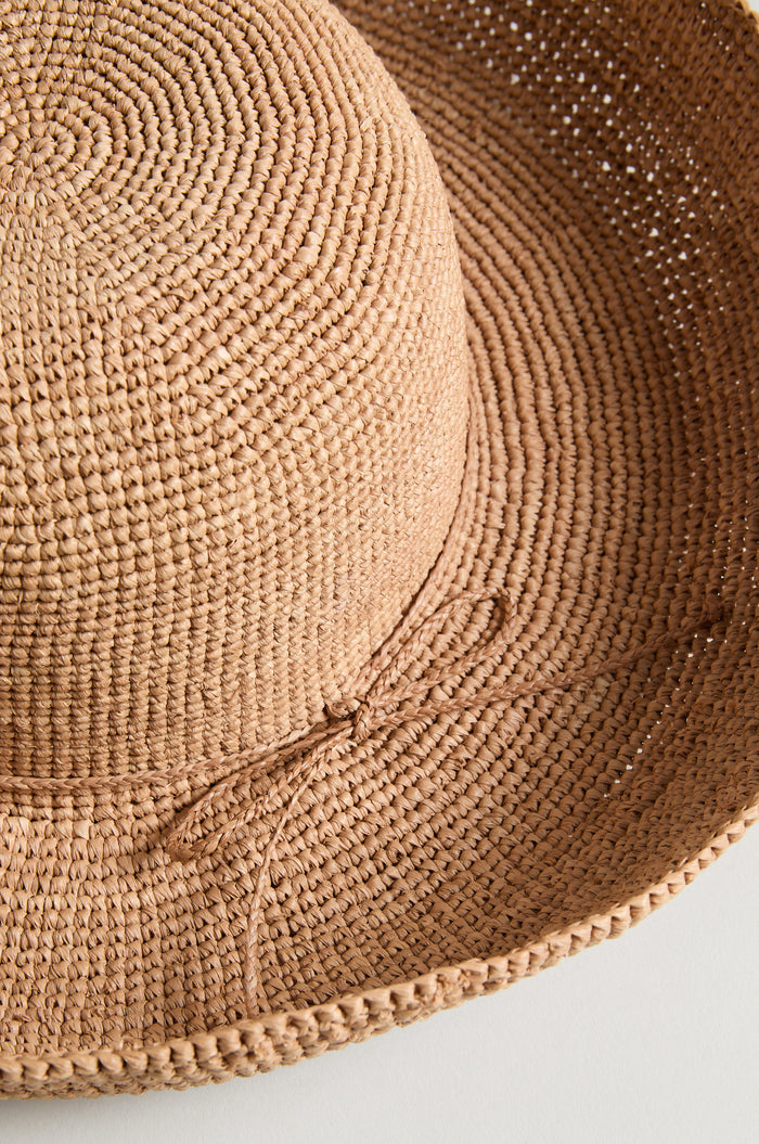 A close-up of the Handwoven Raffia Tie Hat, featuring a wide brim and simple bow detail, displayed on a light background.