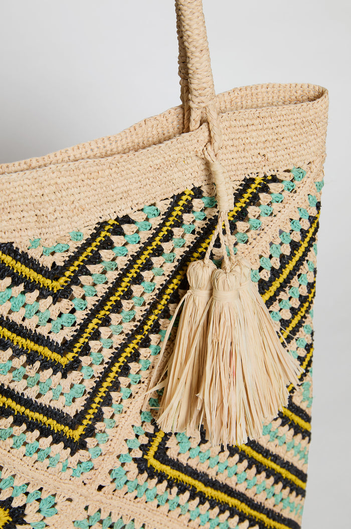 Close-up of the Handwoven Raffia Tote Bag, crafted in Madagascar with black, yellow, and turquoise geometric patterns and two tassels on the handle.