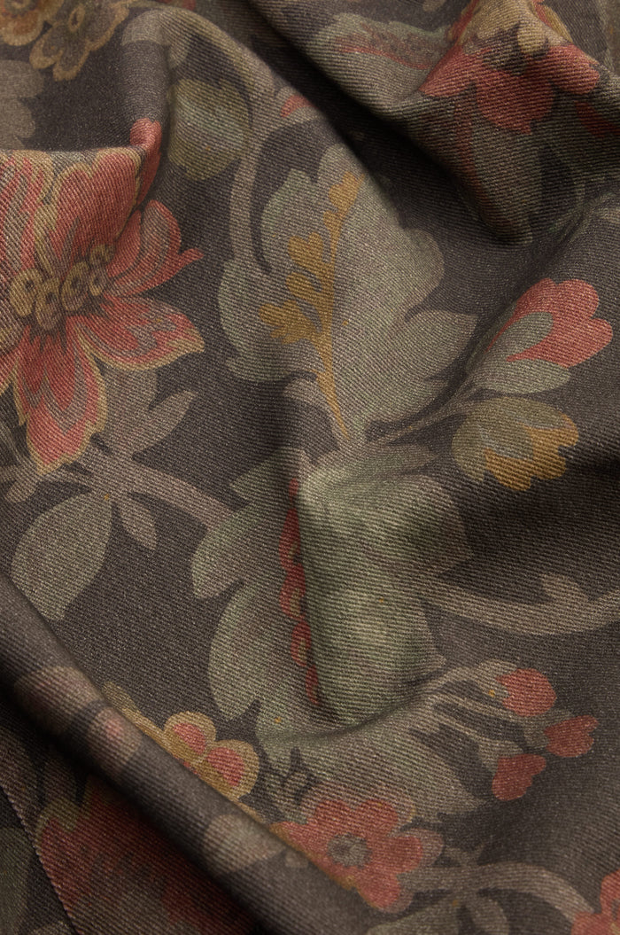 Detail view of the Heirloom Damask Denim Jacket, highlighting its pure cotton fabric adorned with a muted floral pattern in shades of brown, green, and red—reminiscent of a vintage archive print—with subtle wrinkles and folds enhancing its timeless character.