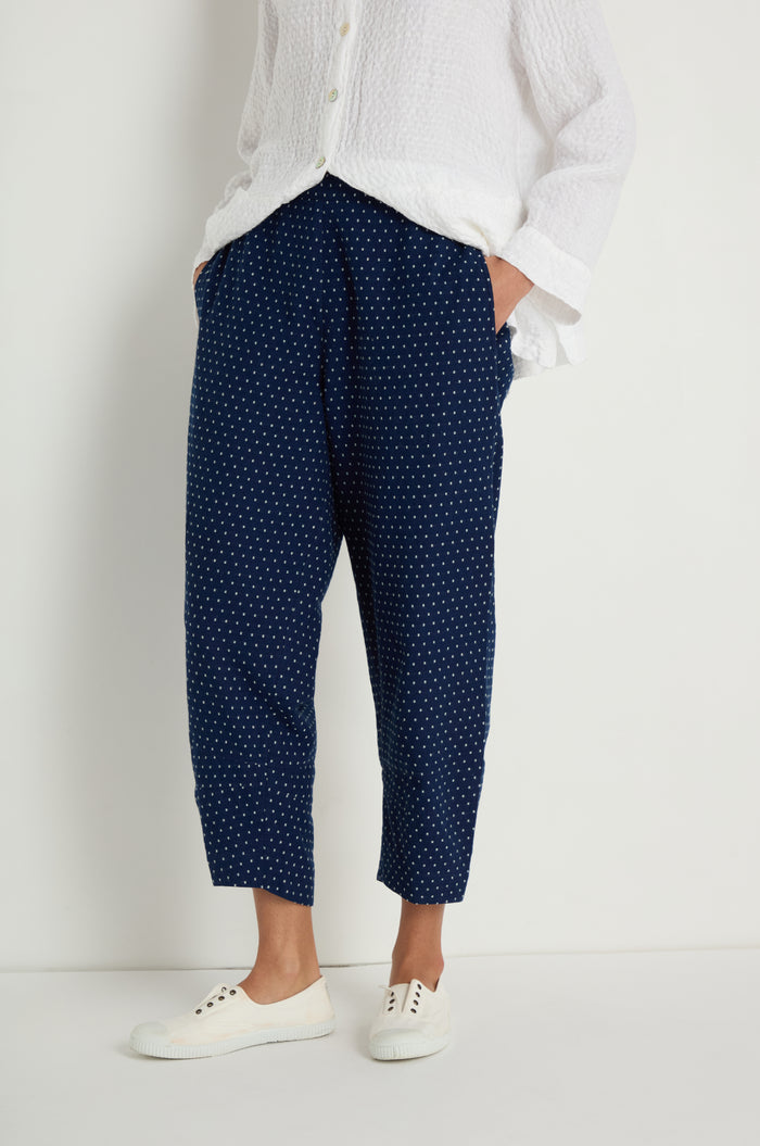 A person wearing a white textured shirt, Indigo Spot Cotton Bubble Trouser with an elasticated waist, and white sneakers stands against a plain white background.