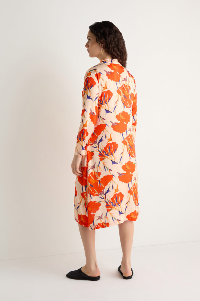 A woman stands sideways against a white background, wearing the knee-length Japanese Floral Shirt Dress with long sleeves and a bold red and purple floral pattern, paired with black slip-on shoes.