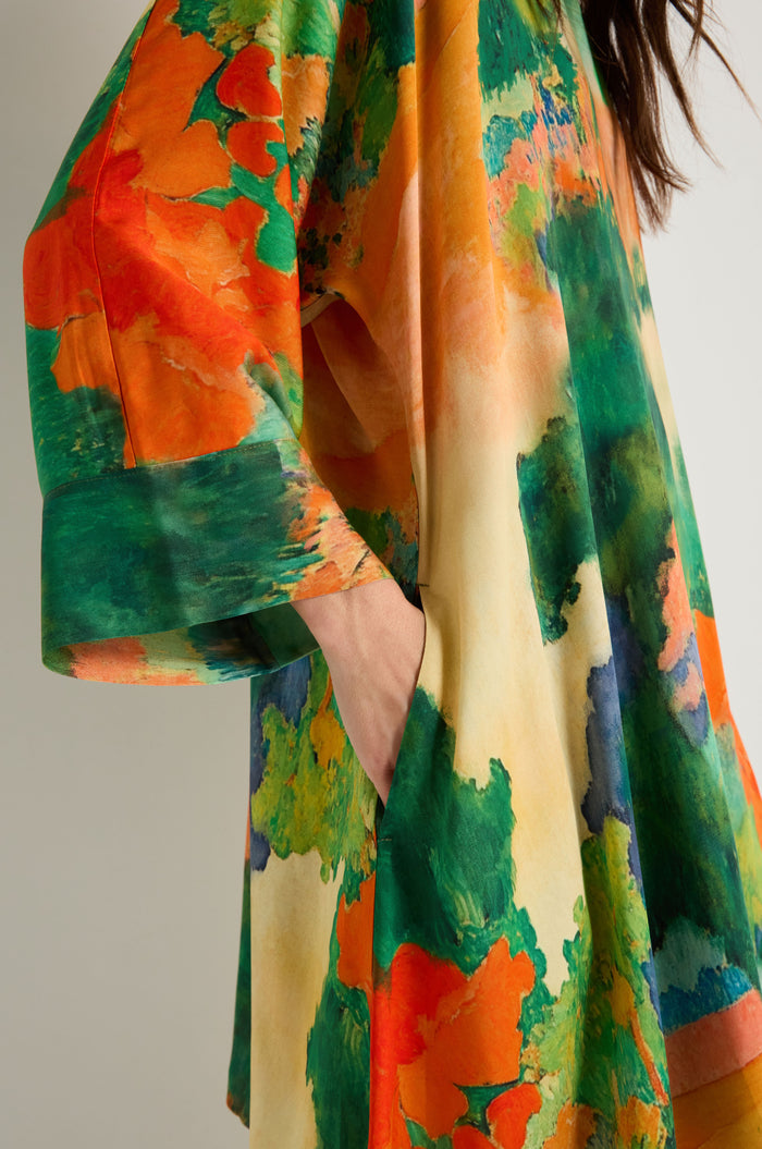 A person is shown from shoulder to thigh wearing the Japanese Garden Boxy Tunic, an oversized woven viscose piece with vibrant orange, green, yellow, and blue abstract patterns.