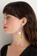 A brown-haired woman wears Kandinsky Sphere Earrings—sculptural, handmade in Paris, with blue, yellow, white, and black elements—shown in profile against a plain light background.