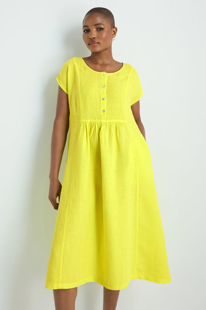 A person models the Linen Button Lemon Placket Dress, featuring a loose fit, short sleeves, buttoned front, and midi length in yellow linen, standing against a white background for an effortlessly elegant look.