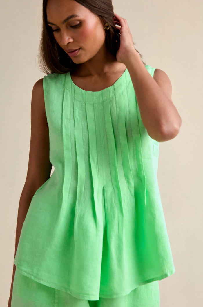 A woman wearing the Linen Pleat Front Pistachio Vest stands against a plain background, touching her hair.