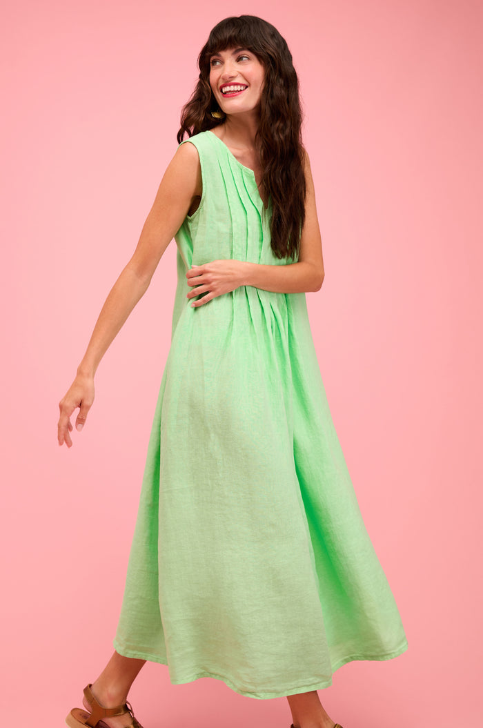 A woman models the Linen Pleat Front Sleeveless Dress in light green with sandals against a plain pink background—a perfect, effortless summer staple.