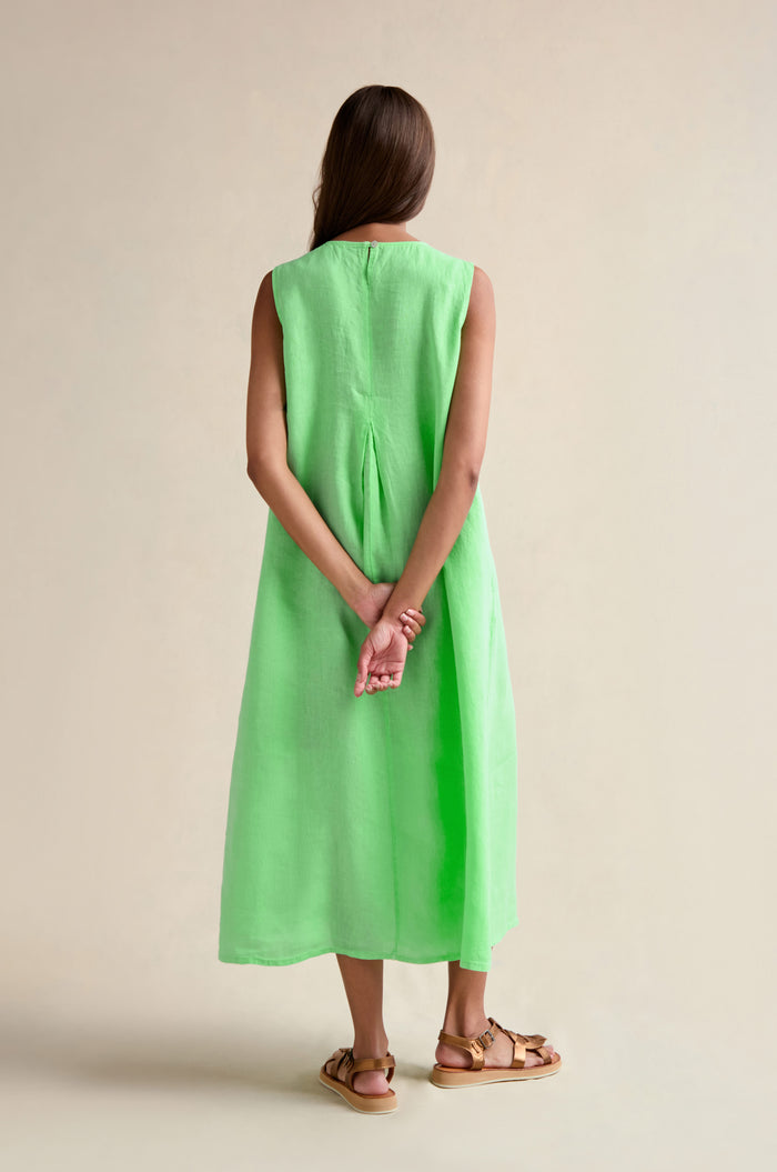 A woman, with her back to the camera, wears the Linen Pleat Front Sleeveless Dress in mint green paired with brown sandals—her hands clasped behind her, showcasing this perfect summer staple.