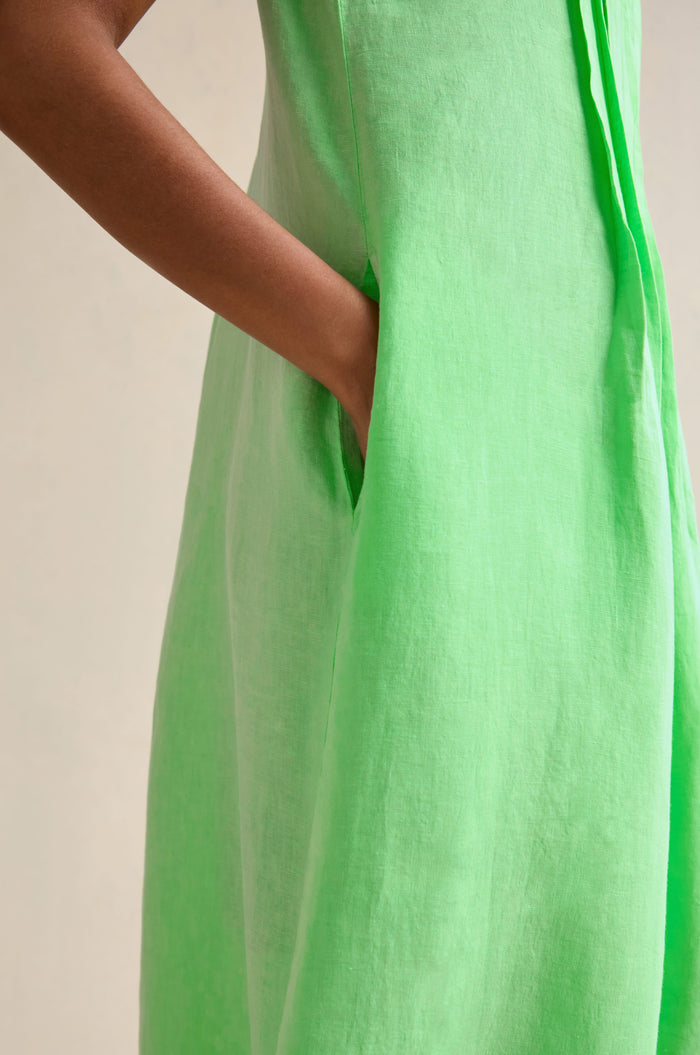A person wearing the Linen Pleat Front Sleeveless Dress in light green stands with one hand in the pocket against a neutral background, highlighting this effortless summer staple.
