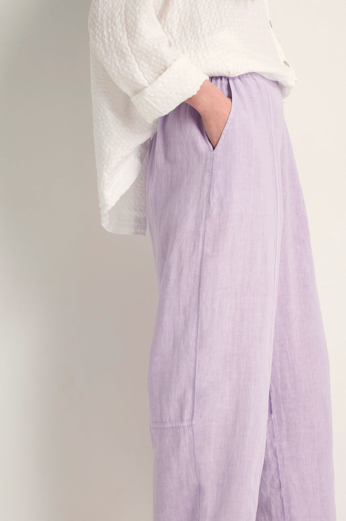 Person stands with one hand in the pocket of Linen Seam Detail Lilac Bubble Trousers featuring a loose fit and elasticated waist, paired with a textured white long-sleeve shirt.