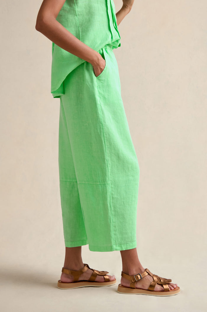 A person stands with one hand in their pocket, wearing the Linen Seam Detail Pistachio Bubble Trouser with an elasticated waistband and brown sandals against a neutral background.