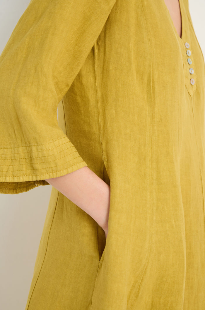 A person wearing the Linen Seam Golden Flare Dress, featuring three-quarter sleeves, panel seams, a buttoned neckline, and side pockets, casually places one hand in a pocket.
