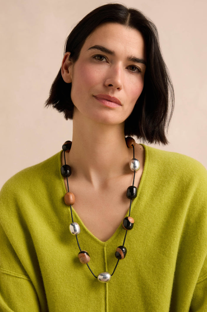 A woman with short dark hair, wearing a lime green sweater and the Long Allsorts Necklace, poses against a neutral background.