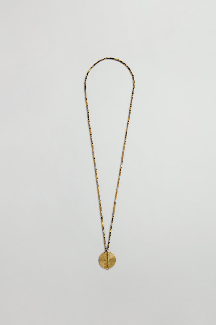 The Long Mini Spiral Bead Pendant is a brass necklace with a thin chain and spiral bead pendant, inspired by handmade Indian jewelry, displayed on a plain white background.
