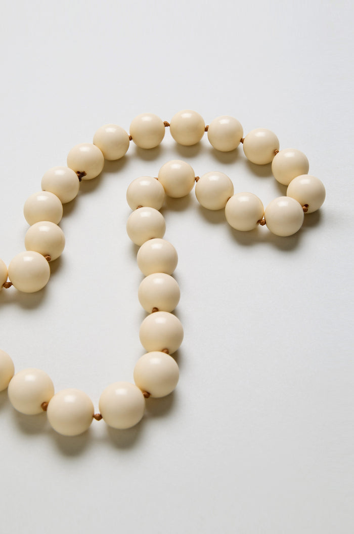 A close-up of the Long Spheres Necklace, showcasing large cream-colored resin sphere beads arranged in a loose curve on a light background.