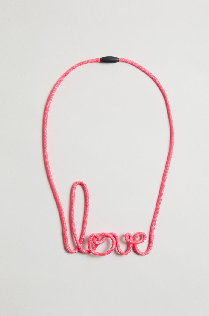 The Love Necklace is a handmade pink cord necklace shaped to spell "love," shown on a simple light background.