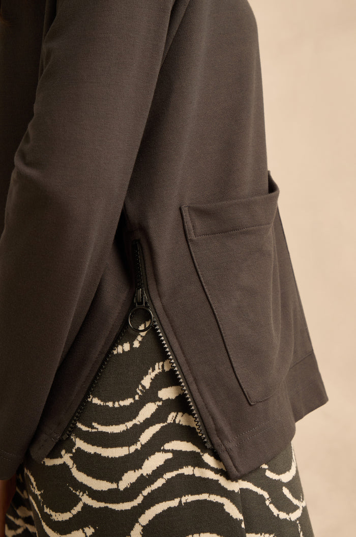 Close-up of a person wearing the Luxe Viscose Jersey Cowl Neck Top with a side zipper and pocket, paired with a patterned black-and-white skirt.