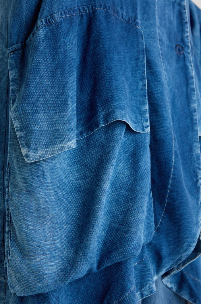 Close-up of the Lyocell Utility Jacket in blue, showcasing its relaxed silhouette, large pocket, visible seams, and a washed finish.