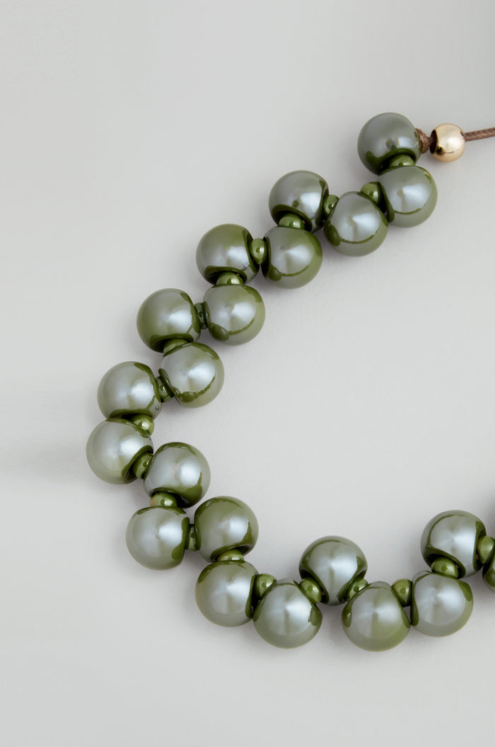 The Macrame Resin Bead Necklace showcases large, glossy olive green resin beads on an adjustable cord, displayed against a light gray background.