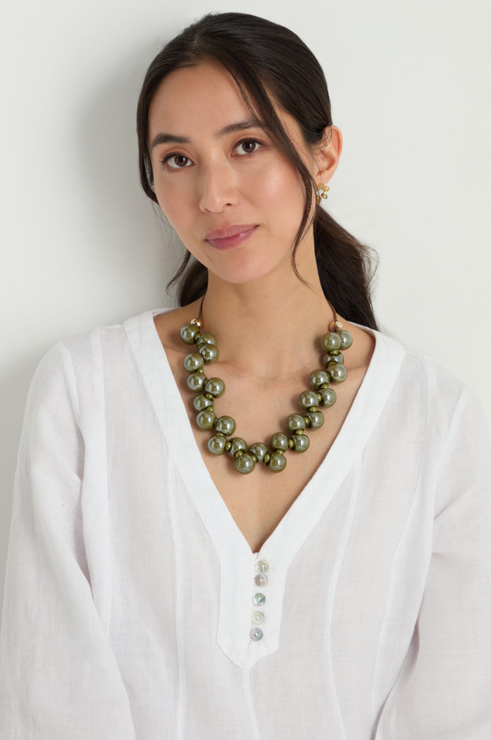 Woman wearing the Macrame Resin Bead Necklace, featuring chunky green resin beads and an adjustable cord, styled with a white blouse against a plain light background.