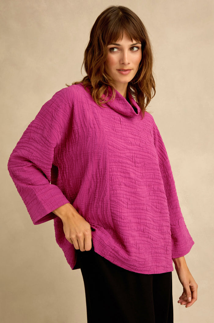 A woman stands against a neutral background wearing a Magenta Wave Textured Crinkle Cowl Neck Top with three-quarter sleeves and black pants.