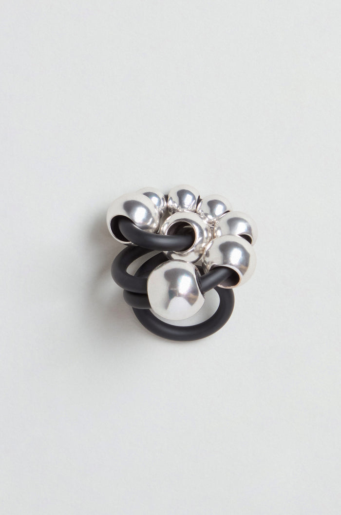 The Metal Spheres Adjustable Ring features large silver beads interwoven with thick black bands, displayed on a simple light background to highlight its sculptural, striking, and sophisticated modern design.