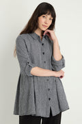 A woman stands against a light background wearing a long-sleeved Micro Gingham Shirt, featuring rolled sleeves and crafted from a linen-viscose blend.