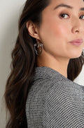 A woman with long brown hair, dressed in a checkered blazer, glances over her shoulder while wearing the sculptural Mini Faces Earrings—abstract face-shaped earrings.