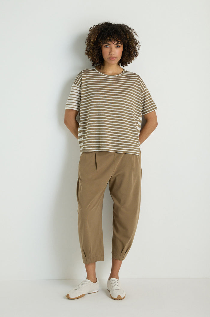 A person stands against a plain background, hands in pockets, wearing the Mixed Stripe T-Shirt made from a linen and viscose blend, tan cropped pants, and white sneakers.