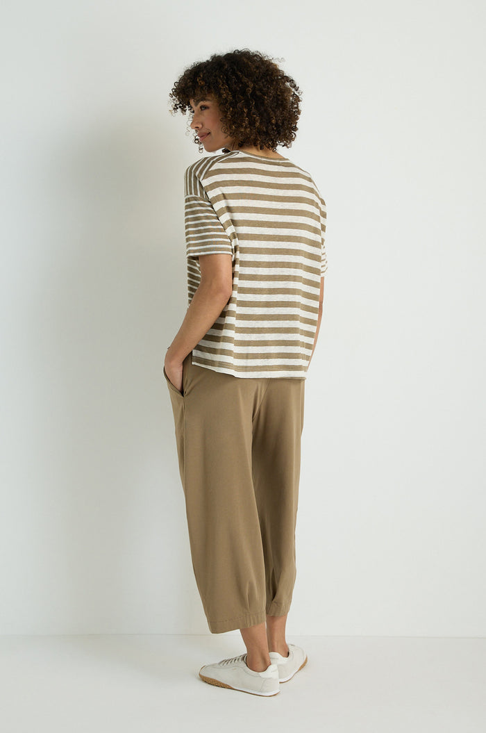 A person stands facing away, wearing the Mixed Stripe T-Shirt, loose brown pants, and white sneakers against a plain white background.