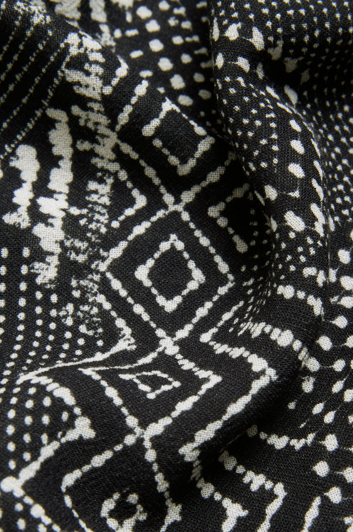 Close-up of the Mono Patchwork Ikat Dress fabric, showcasing white geometric patterns—including dots, diamonds, and lines—on a monochrome background with slight folds that enhance its textured appearance.