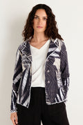 A woman with long curly hair stands against a plain light background wearing the Monochrome Patchwork Jersey Jacket over a white cotton top and black pants.