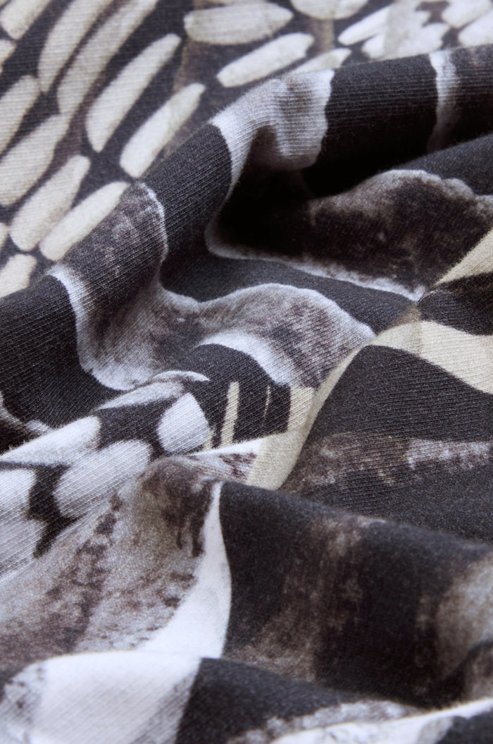 Close-up of black, white, and beige patterned fabric with a slightly wrinkled texture and organic shapes resembling scales or feathers, characteristic of the pure cotton Monochrome Patchwork Jersey Jacket.