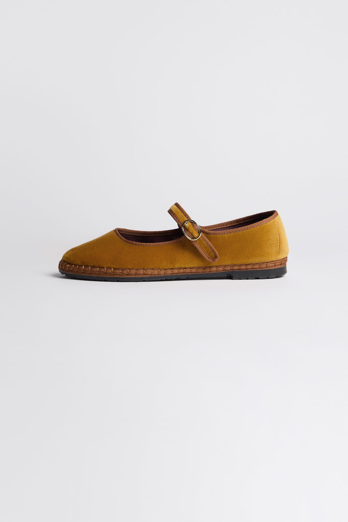 The Mustard Mary Jane Velvet Shoes feature a brown buckle strap and sole, displayed in profile on a white background, showcasing sustainable craftsmanship inspired by traditional Spanish shoemaking.