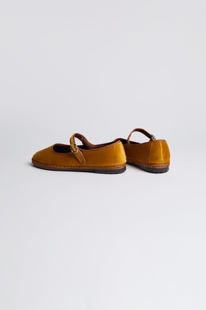 The Mustard Mary Jane Velvet Shoes, featuring buckle straps, brown trim, and rubber soles, crafted with traditional Spanish shoemaking techniques, are displayed on a light background.