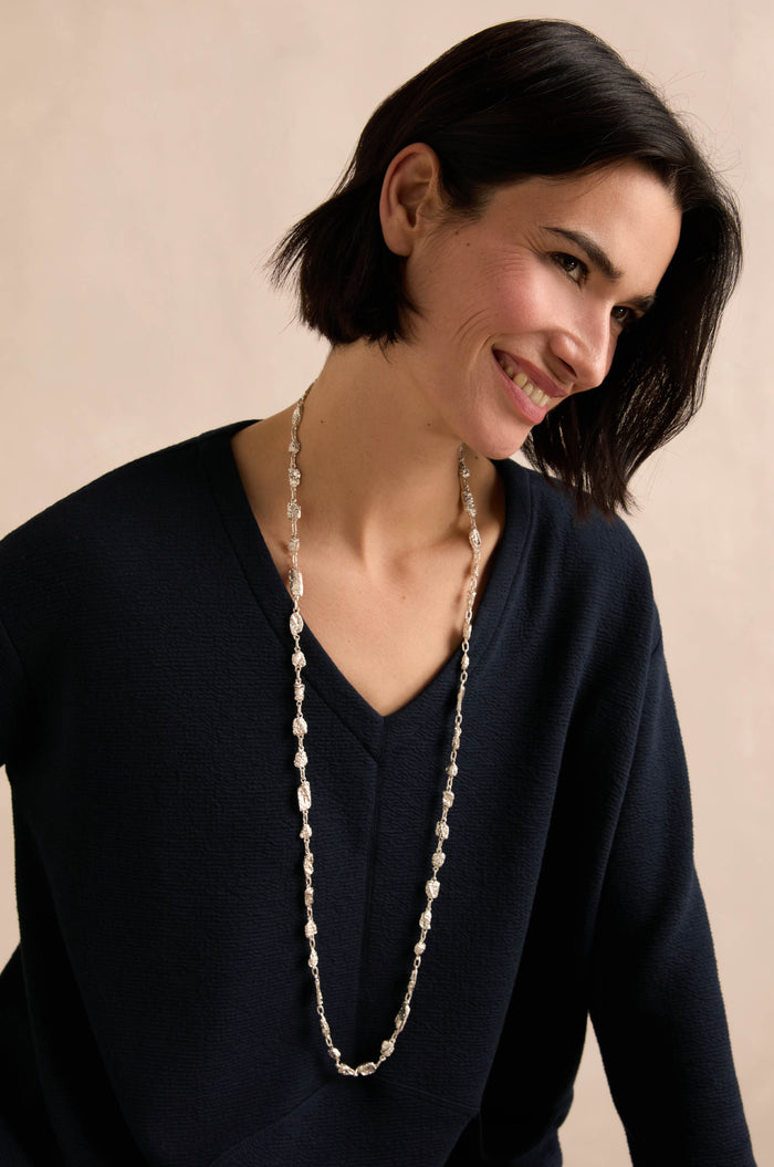 Wearing the Nugget Chain Necklace over a dark V-neck sweater, a woman with short dark hair smiles and looks slightly to the side against a neutral background.