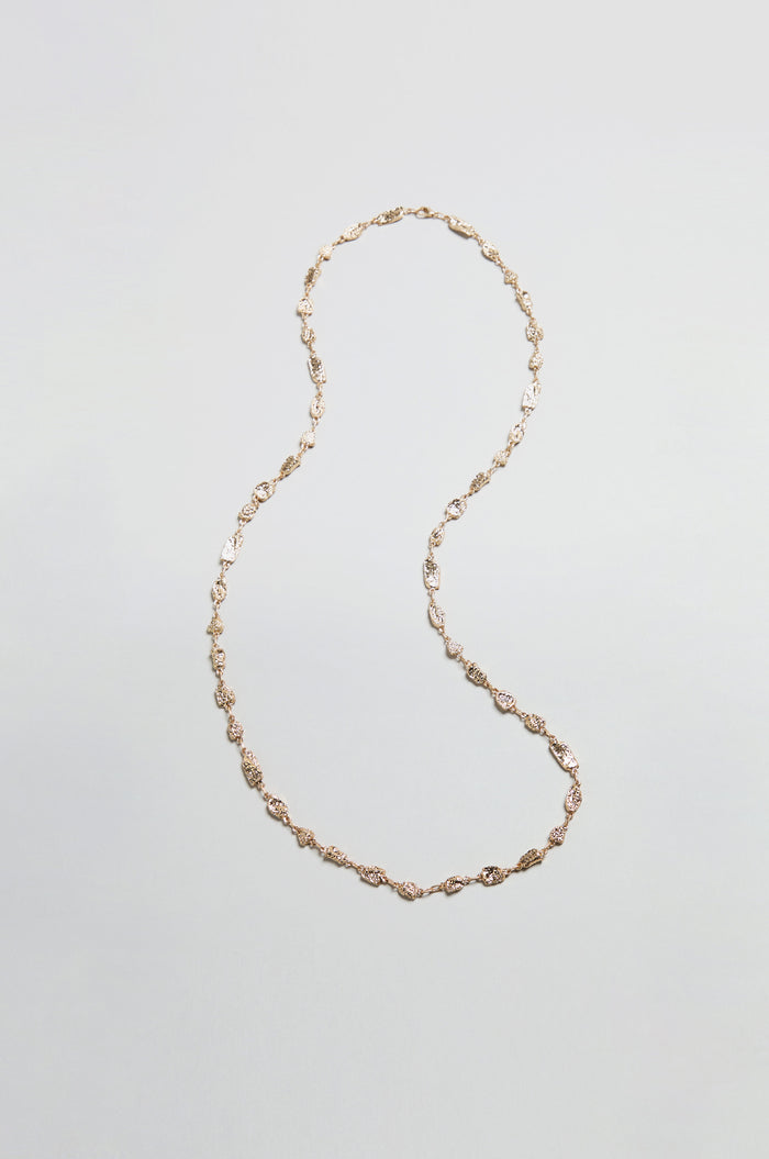 The Nugget Chain Necklace, featuring twisted links and a textured gold surface, is arranged in an S-shape on a plain, light gray background.
