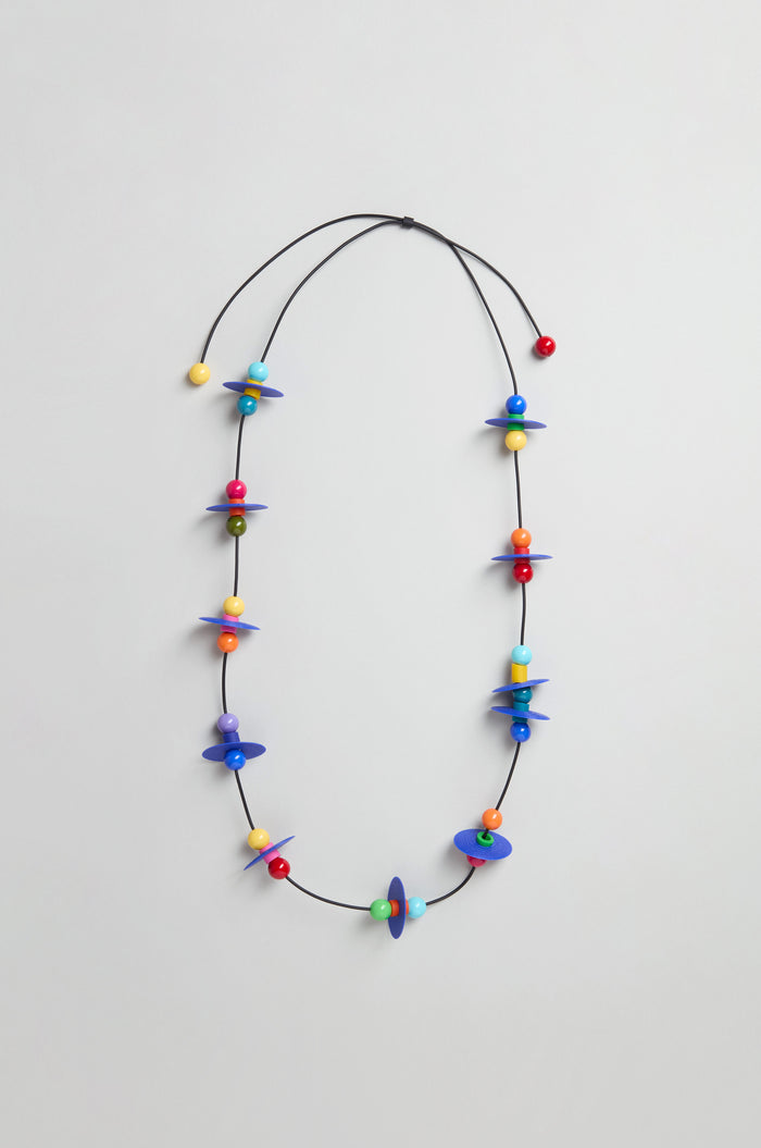 The Orbit Necklace showcases an abstract geometric design with multicolored beads and blue discs on a thin black cord, handmade in Paris.