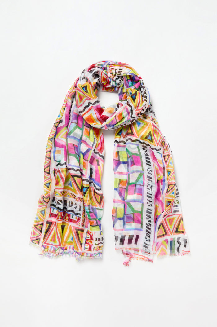 The Painted Geometric Scarf is a lightweight, luxe accessory featuring a colorful geometric pattern of pink, yellow, blue, and green squares and triangles on a white background.