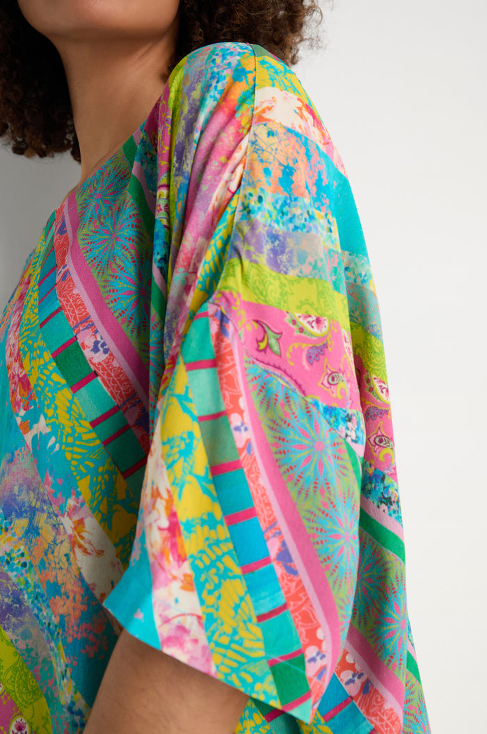A person is wearing the Patchwork Stripe Boxy Top, featuring colorful stripes in blue, pink, green, and yellow with a boxy fit and short sleeves. Only part of their face and shoulder are visible.