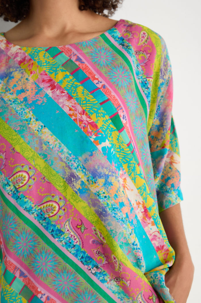 A person wearing the Patchwork Stripe Boxy Top featuring diagonal stripes with paisley and floral designs in pink, green, yellow, and turquoise archive prints for a vibrant look.