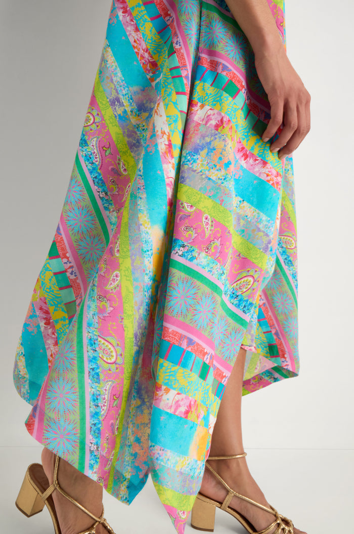 A person in the Patchwork Stripe Summer Dress, featuring colorful stripes in viscose crepe, and gold high-heeled sandals stands against a plain white background.