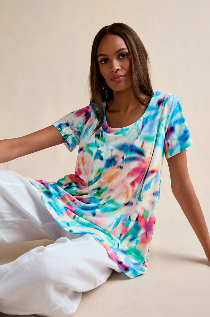 A woman sits on the floor in a relaxed fit, multicolored Petal Haze Jersey Tunic and loose white pants against a neutral background.