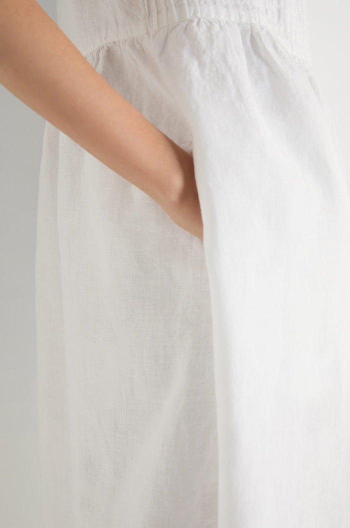 A person wearing a white Pleat Front Linen Bubble Dress has their hand in the dress pocket, shown from the shoulder down against a plain background.