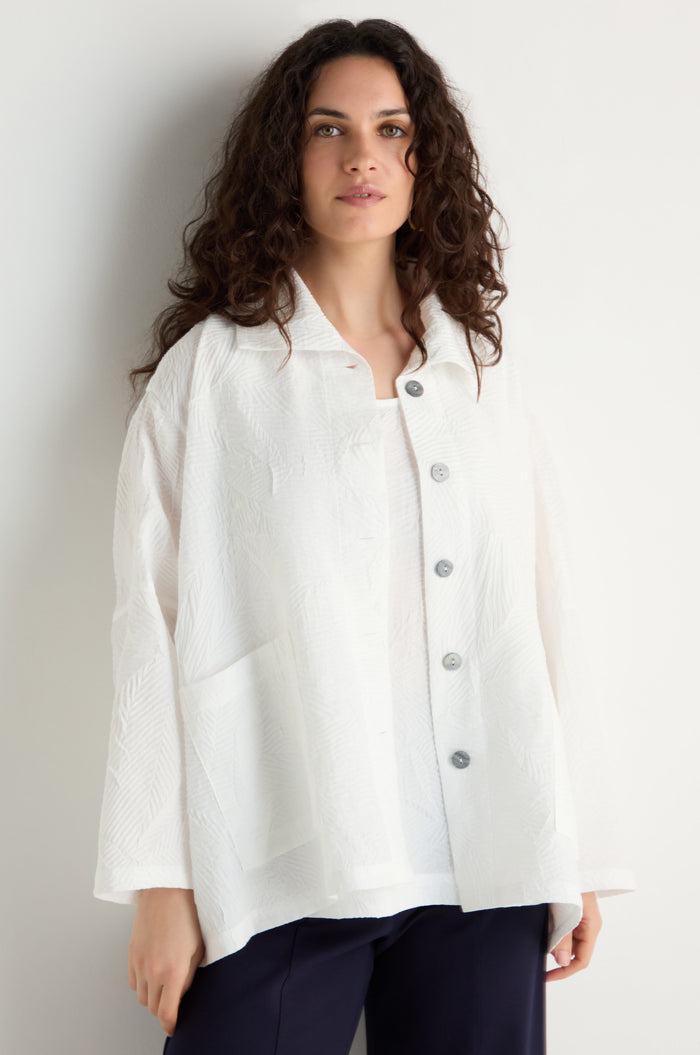 A woman with long curly hair wears the Pleated Leaf Short Jacket in white with dark pants, standing against a plain light background.