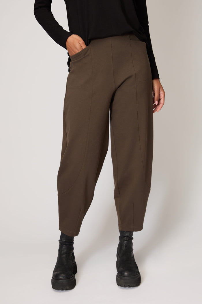 A person wears loose-fitting brown Ponte Bubble Trousers with an elasticated waistband, paired with a black long-sleeve top and black boots, standing against a plain light background.