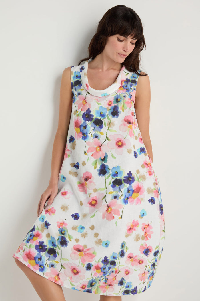 A woman wearing the Primrose Print Sleeveless Linen Dress stands against a plain light background, looking down.