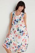 A woman wearing the Primrose Print Sleeveless Linen Dress stands against a plain light background, looking down.