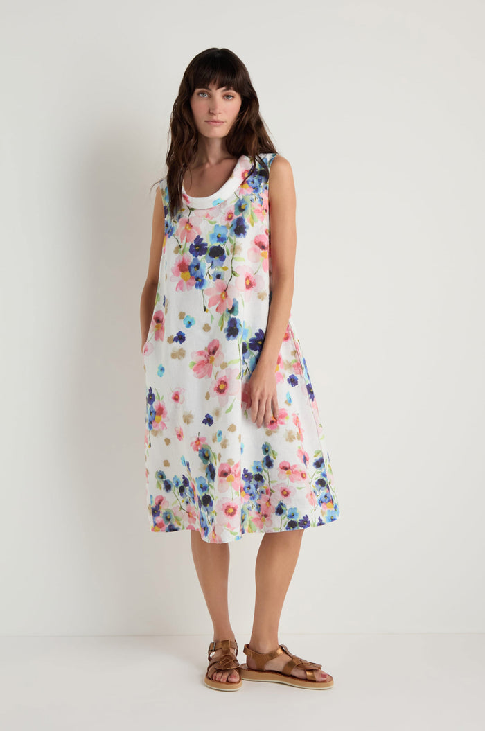 A woman stands against a plain background, wearing the Primrose Print Sleeveless Linen Dress paired with brown sandals.