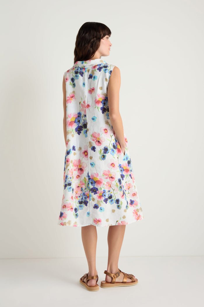 A woman faces away, wearing the Primrose Print Sleeveless Linen Dress with brown sandals.