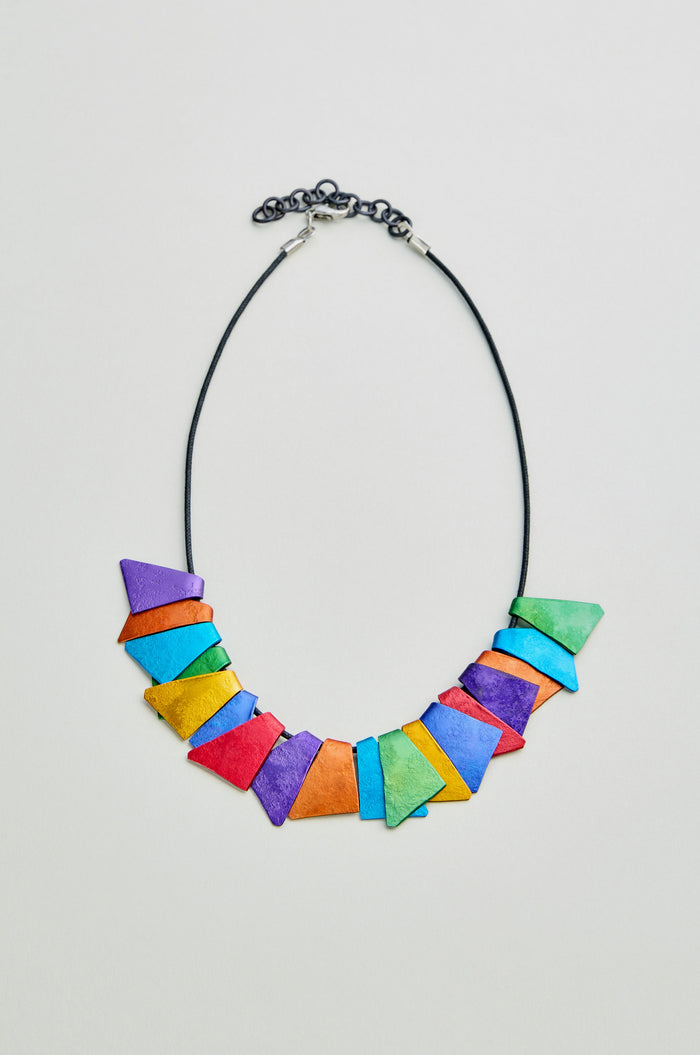 The Mini Segments Necklace features a black cord with bold geometric beads in blue, green, yellow, orange, pink, and purple—an eye-catching accessory.